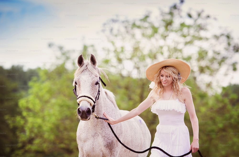 Woman in white dress walking with horse in green countryside