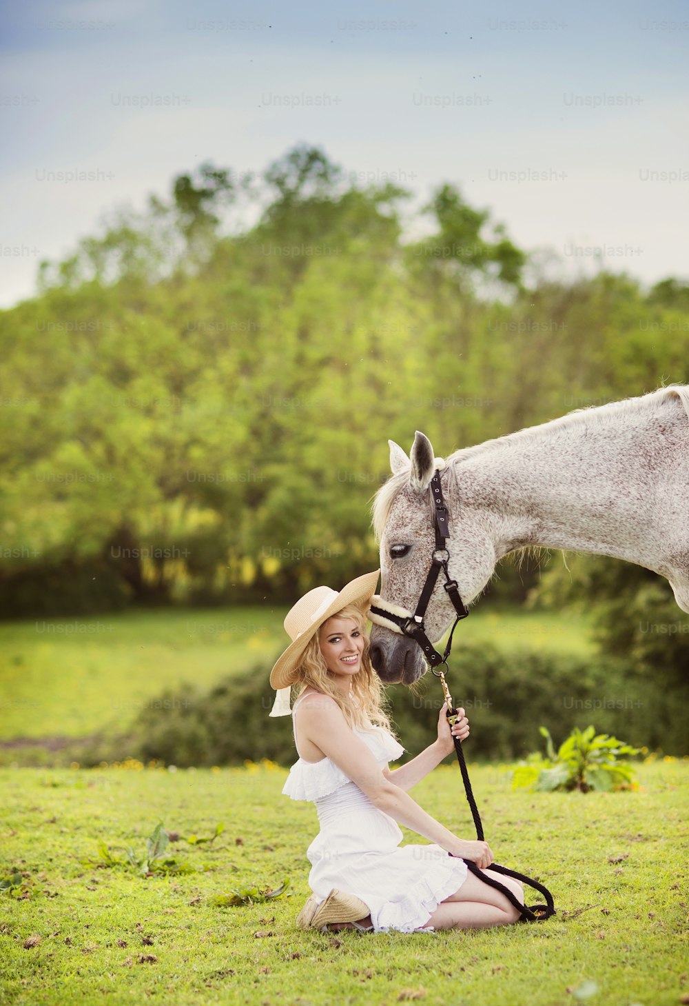緑の田園地帯で馬と歩く白いドレスを着た女性