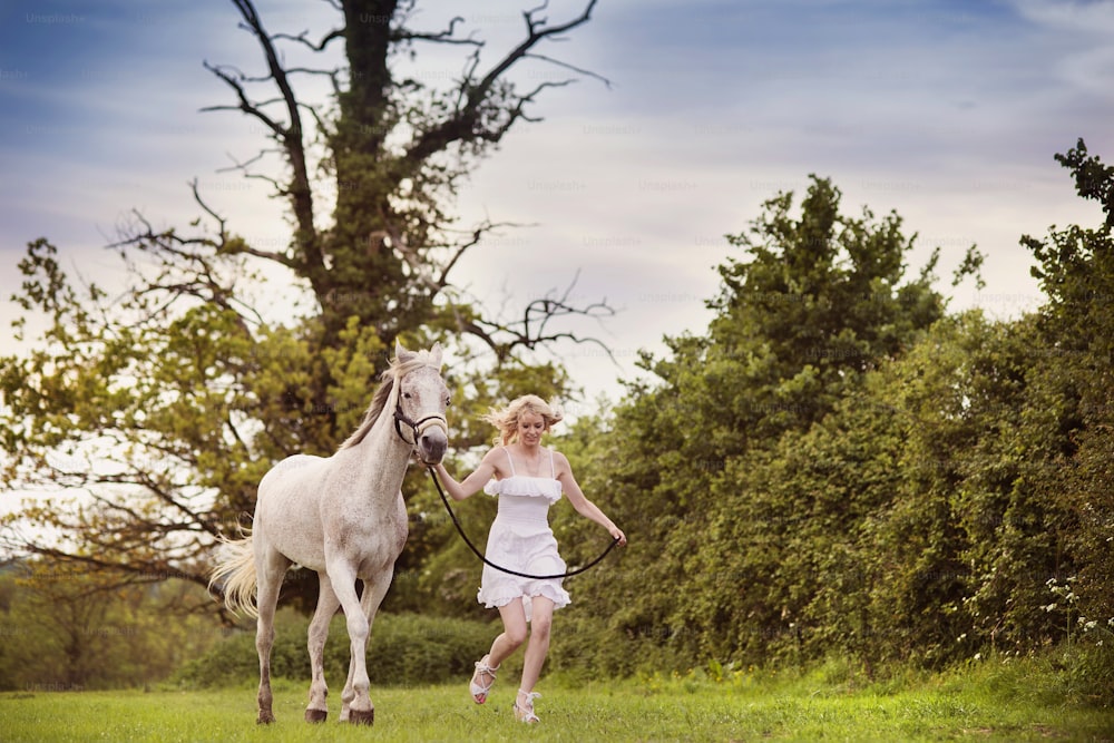 Frau im weißen Kleid geht mit Pferd in grüner Landschaft spazieren