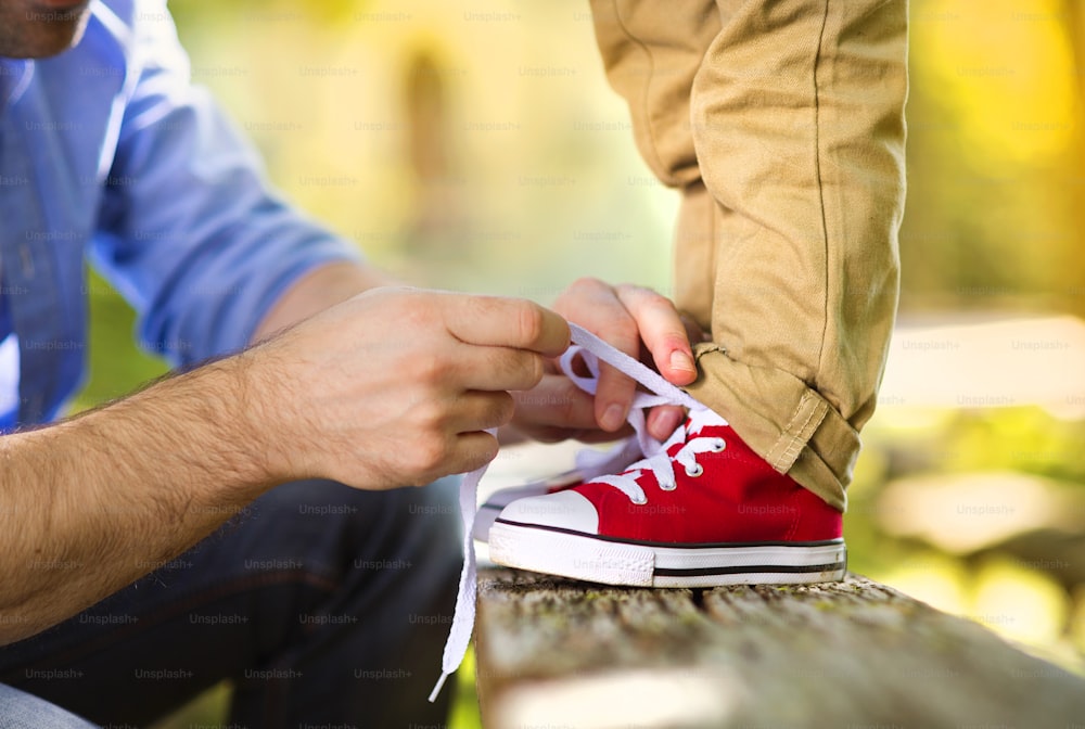 Father is helping his son to tie his shoes in summer nature