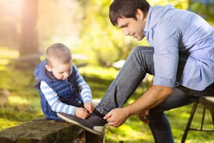 Father and son spending time together in summer nature, little boy is tying his father's shoes