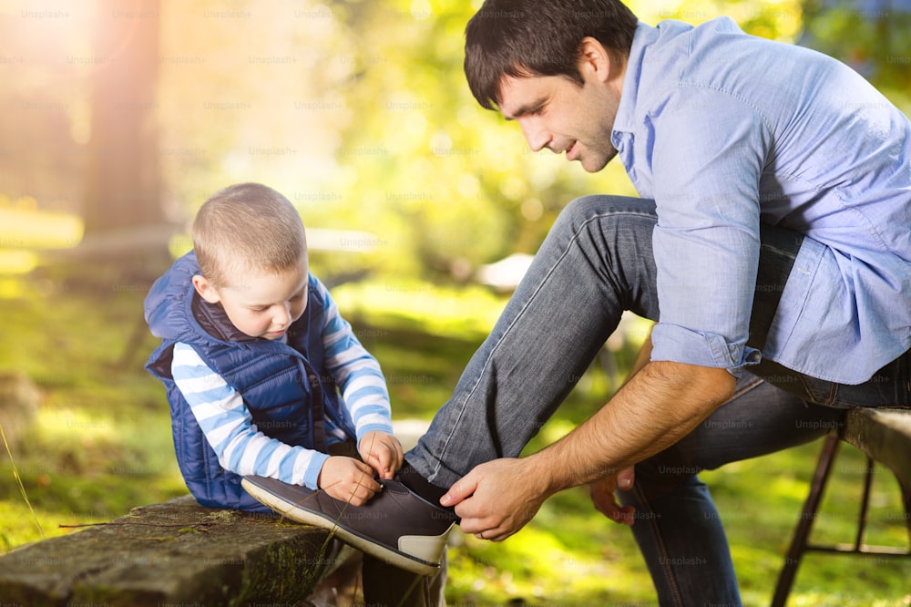 Padre e hijo pasando tiempo juntos en la naturaleza del verano, niño está atando los zapatos de su padre