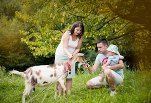 La familia feliz se relaja en un prado verde con cabra