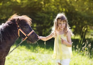 Portrait of tlittle girl having fun at countryside outdoors, feeding pony