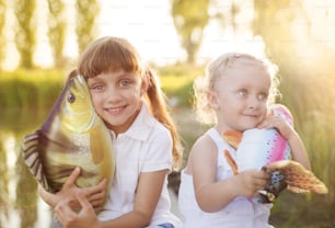 Two cute little sisters with playing with toy fish by the lake
