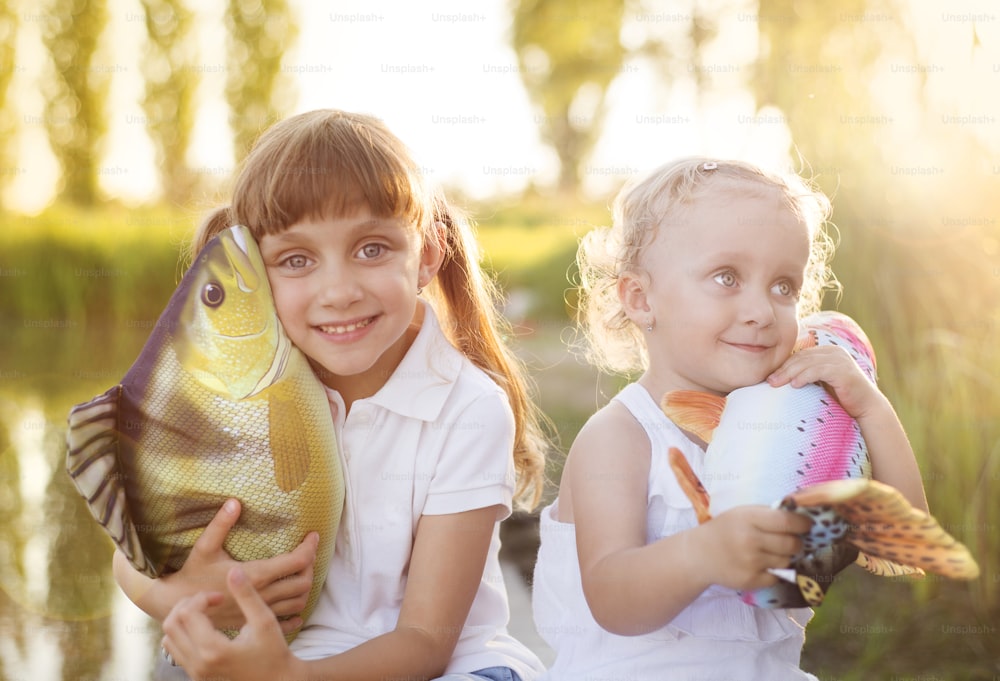 湖畔でおもちゃの魚と遊ぶ2人のかわいい妹
