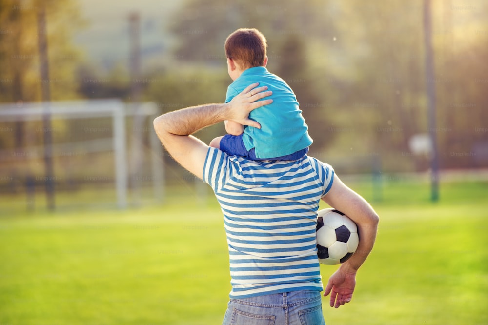 Padre joven con su hijo pequeño divirtiéndose en el campo de fútbol