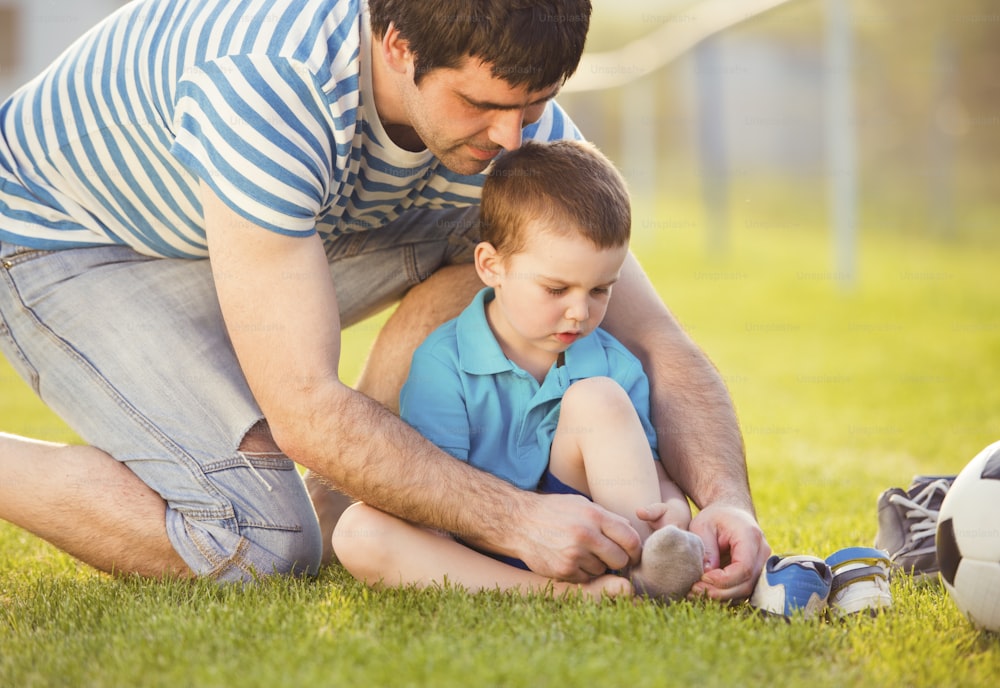 Pai jovem com seu filho pequeno trocando de sapatos no campo de futebol