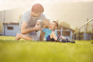 Junger Vater mit seinem kleinen Sohn wechselt die Schuhe auf dem Fußballplatz