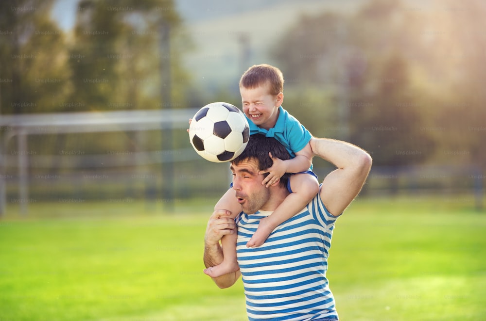 Padre joven con su hijo pequeño divirtiéndose en el campo de fútbol