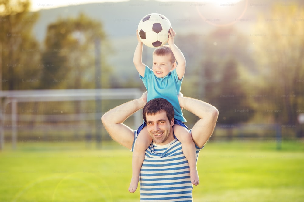 Padre joven con su hijo pequeño divirtiéndose en el campo de fútbol