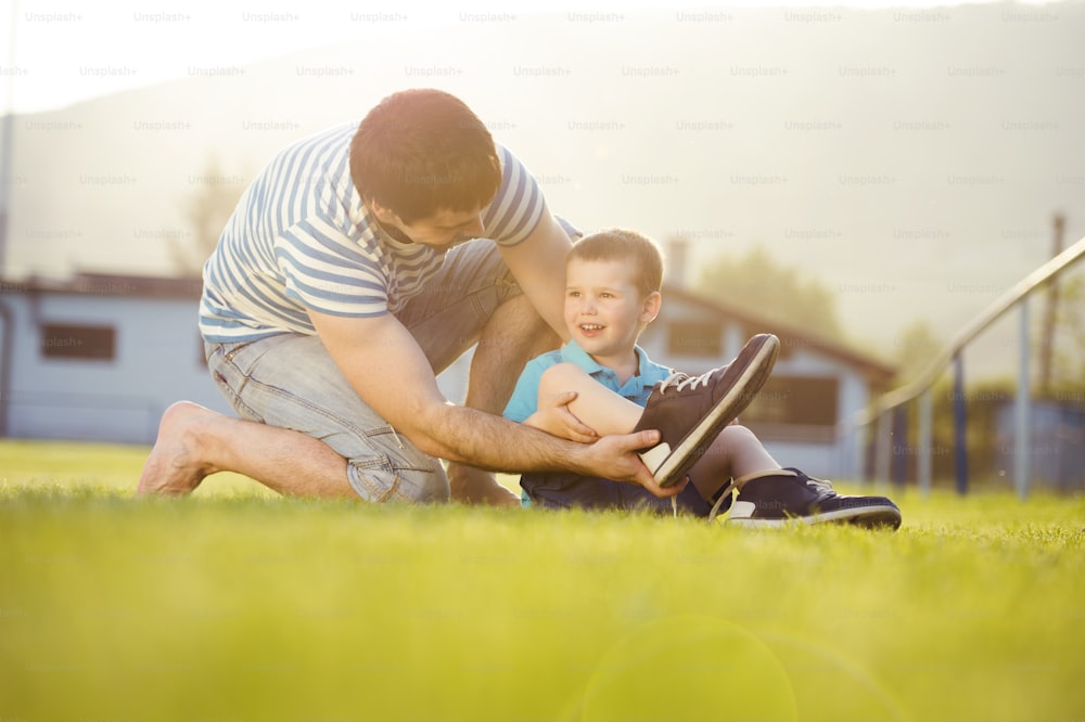 Jeune père avec son petit fils changeant de chaussures sur un terrain de football