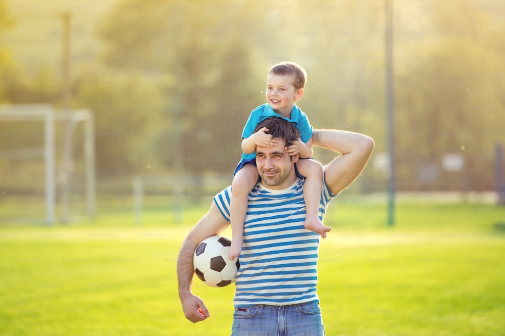 Padre joven con su hijo pequeño divirtiéndose en el campo de fútbol