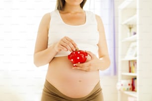 Portrait of unrecognizable pregnant woman measuring holding piggy bank in her hand