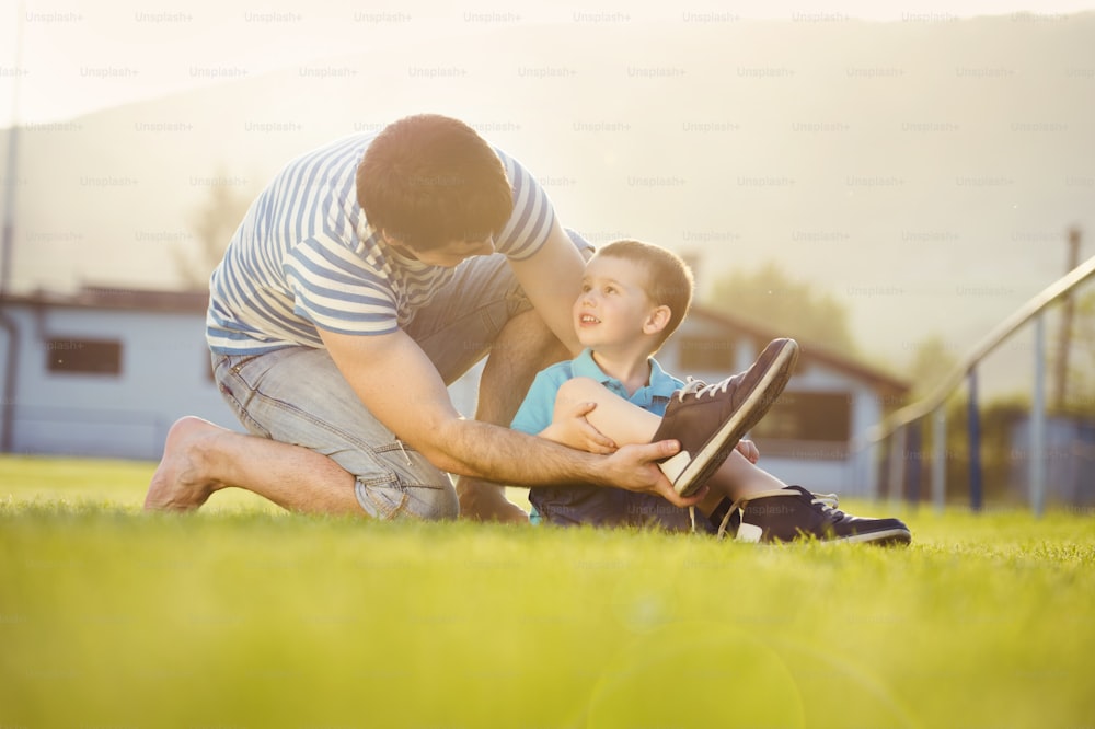 Young father with his little son changing shoes on football pitch