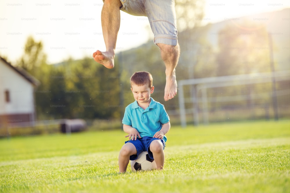 Padre joven con su hijo pequeño jugando al fútbol en el campo de fútbol