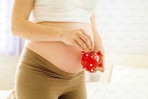 Ritratto di donna incinta irriconoscibile che misura tenendo salvadanaio in mano