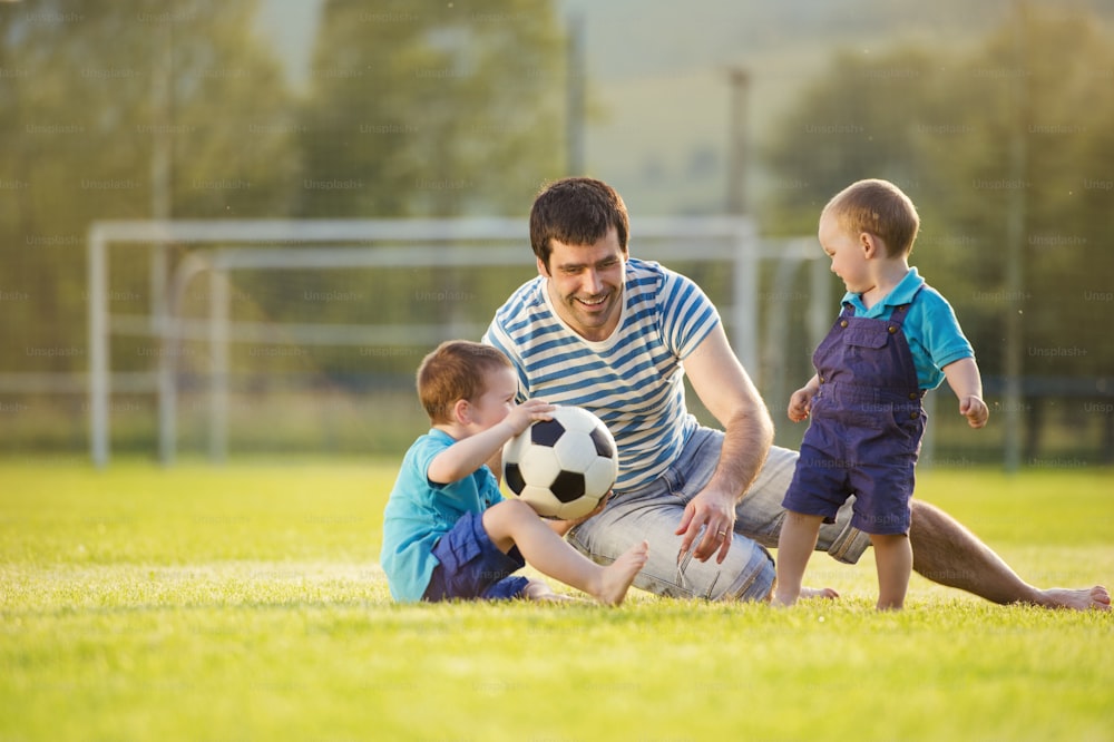Padre joven con sus hijos pequeños jugando al fútbol en el campo de fútbol