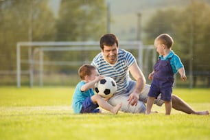 Junger Vater mit seinen kleinen Söhnen spielt Fußball auf dem Fußballplatz