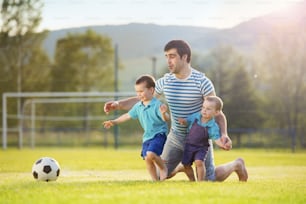 サッカーのピッチでサッカーをする幼い息子を持つ若い父親