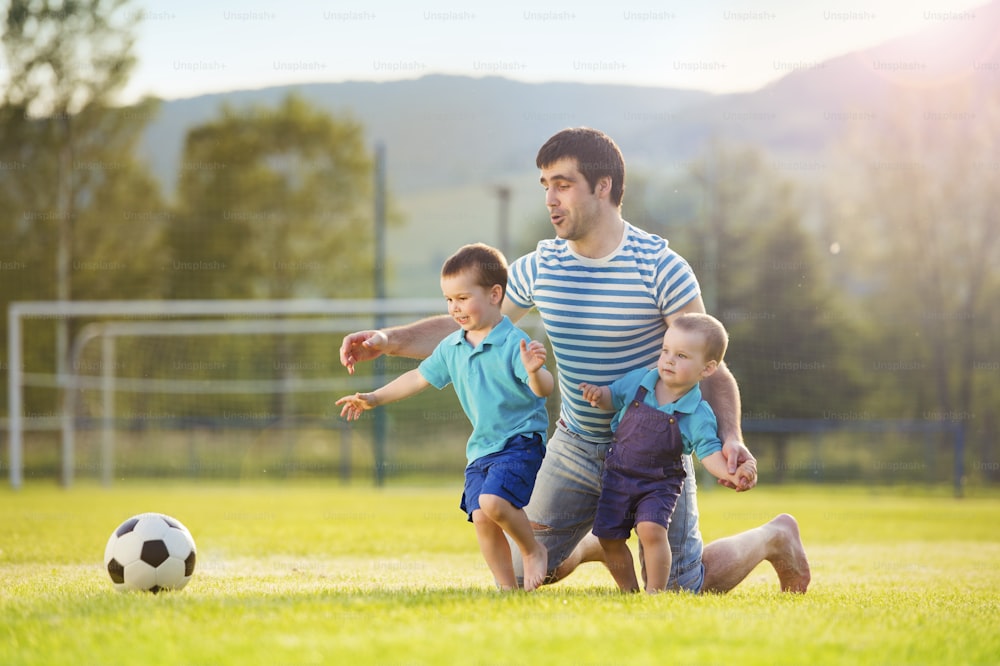 Pai jovem com seus filhos pequenos jogando futebol no campo de futebol