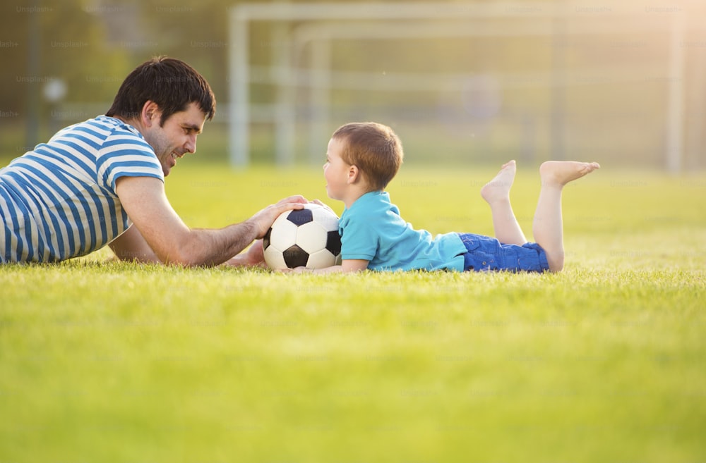Young father with his little son having fun on football pitch