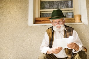 Alter Mann, der die Zeitung vor seinem Haus liest