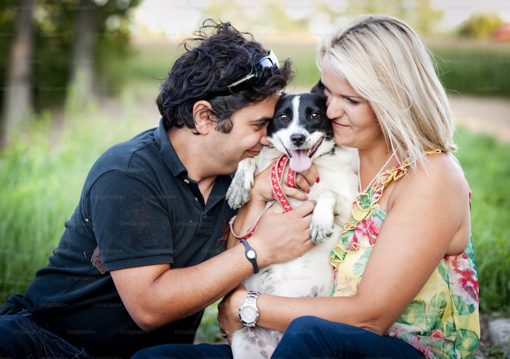 Happy young couple is playing their two dog in green nature