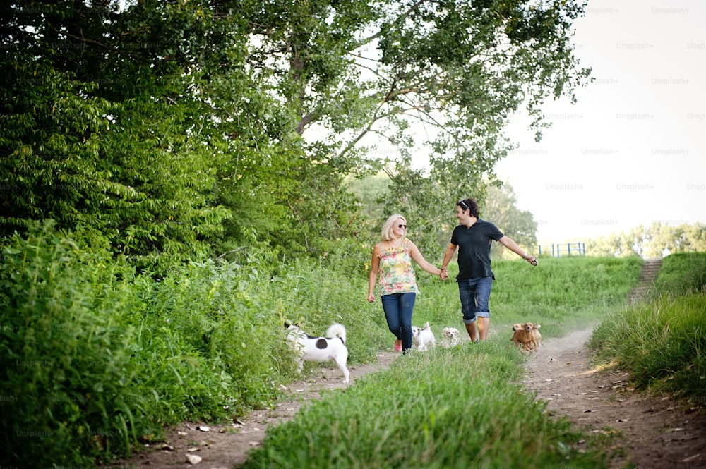 Una joven pareja feliz está paseando a sus dos perros en la naturaleza verde