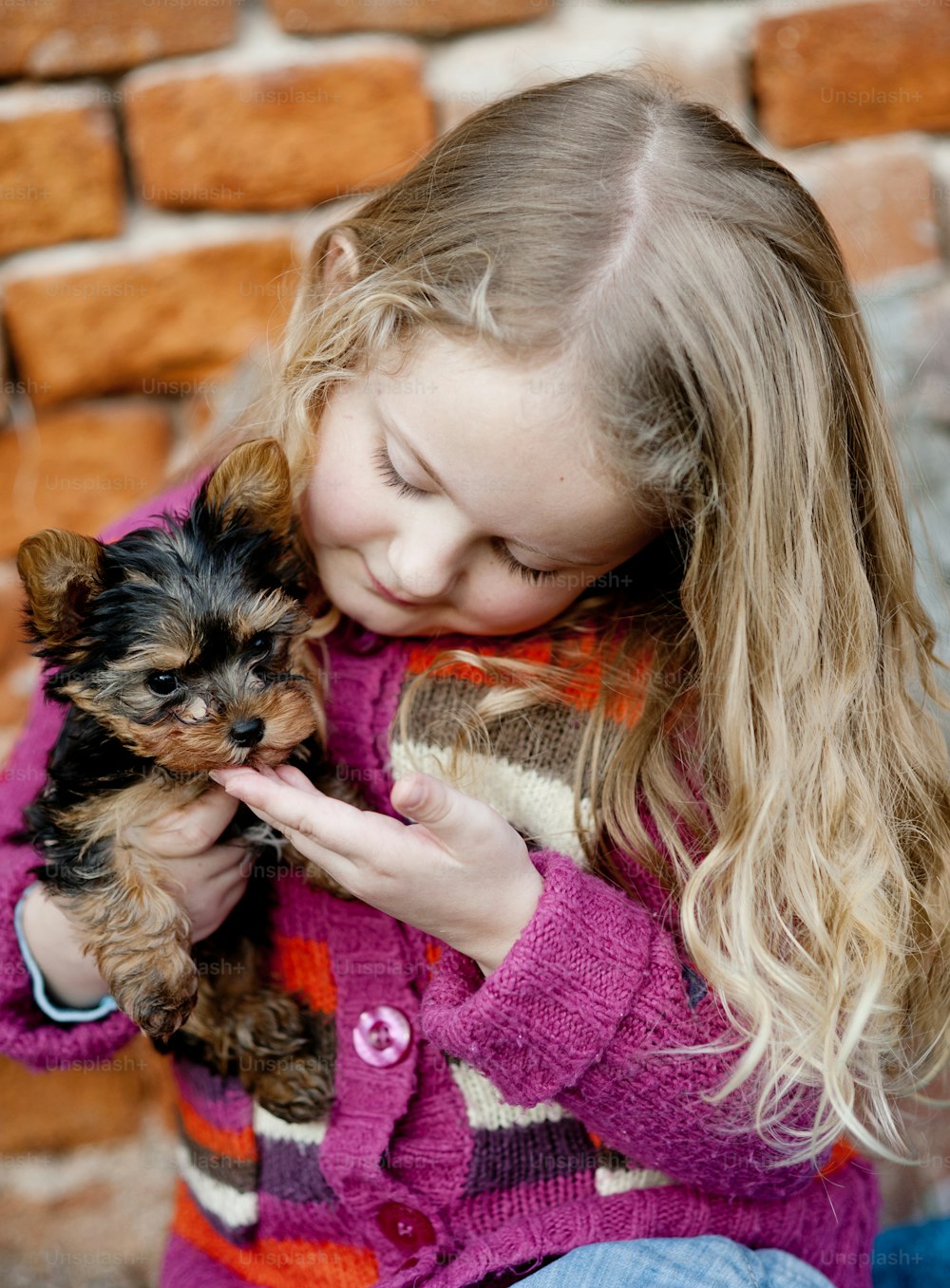 Little girl is playing with her puppy by brick wall
