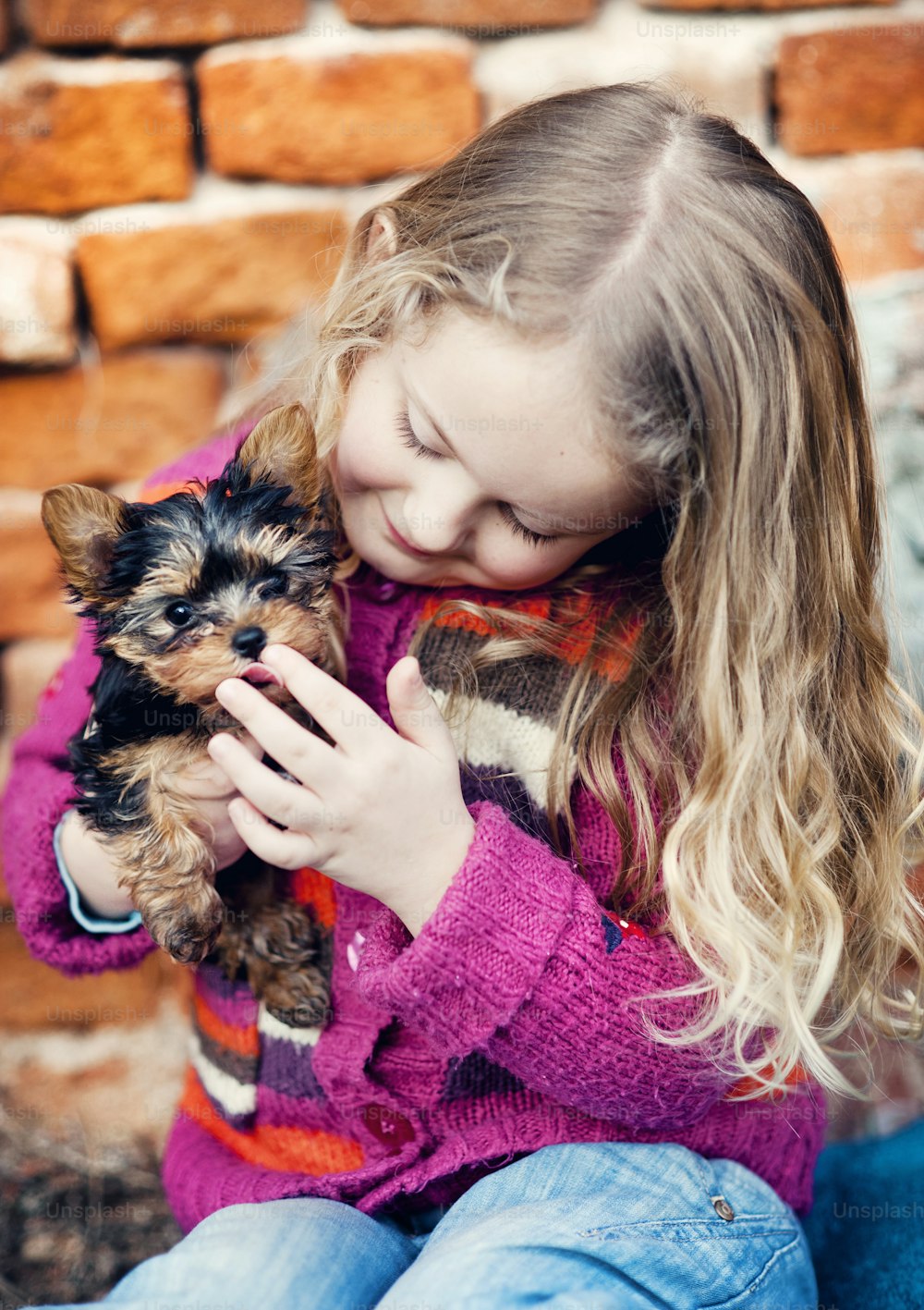小さな女の子がレンガの壁で子犬と遊んでいる