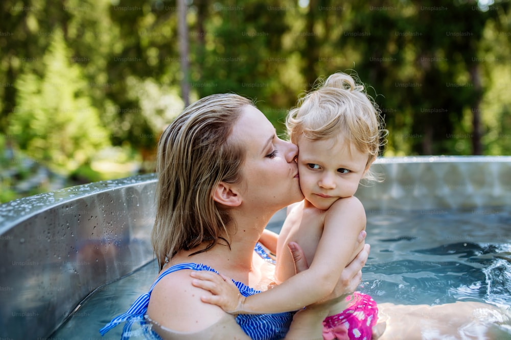 A mother with her little daughter enjoying bathing in wooden barrel hot tub, summer vacation concept.