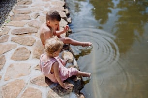 귀여운 소녀와 소년이 호숫가 오솔길에 함께 앉아 물속에 발을 담그고 여름 방학 컨셉을 가지고 있다.