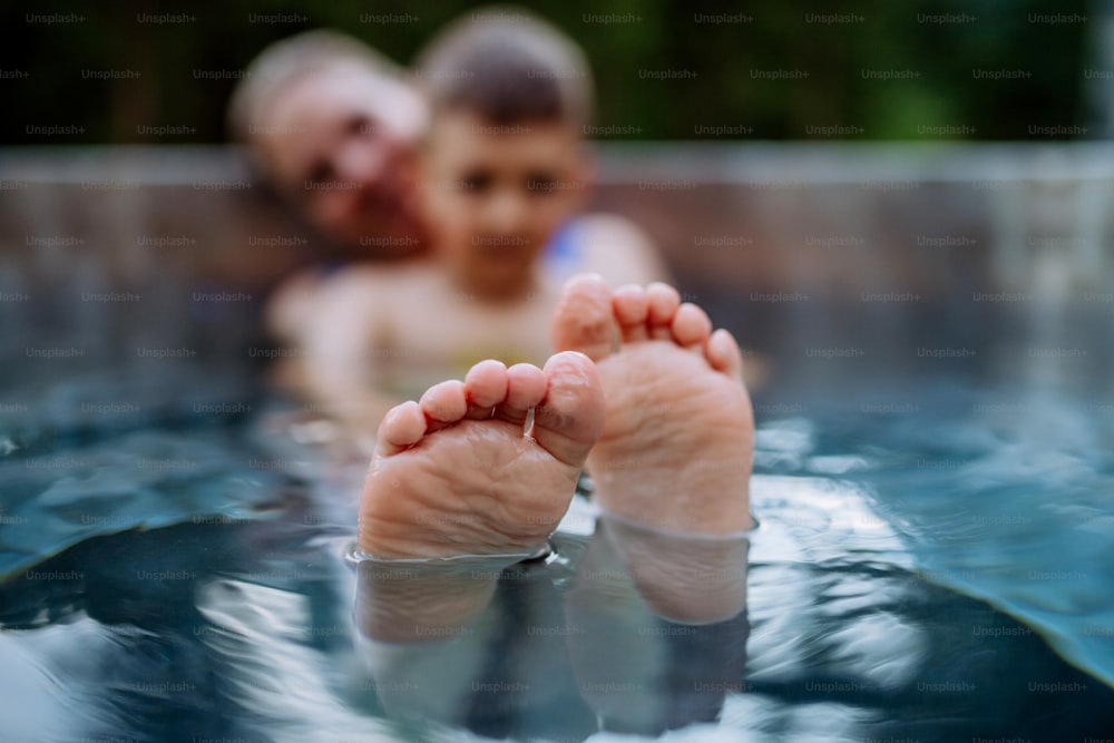 A mother with her little son enjoying bathing in wooden barrel hot tub in the terrace of the cottage, focus on feet.
