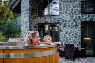 다른 한 명은 작은 아들과 함께 전원주택의 테라스에 있는 나무 온수 욕조에서 목욕을 즐기고 있습니다.