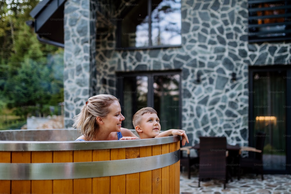 A other with her little son enjoying bathing in wooden hot tub in the terrace of the cottage.