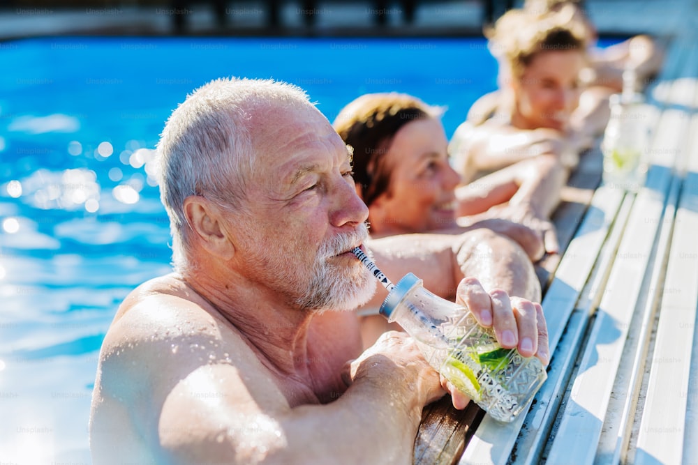 A senior man enjoying cold drink when standing in swimming pool with his family.