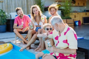 A multi generation family enjoying drinks when sitting at backyard pool.