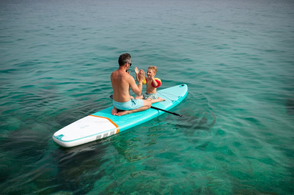 A happy father and little son on paddle board in sea together. Fatherhood and quality time with child concept.