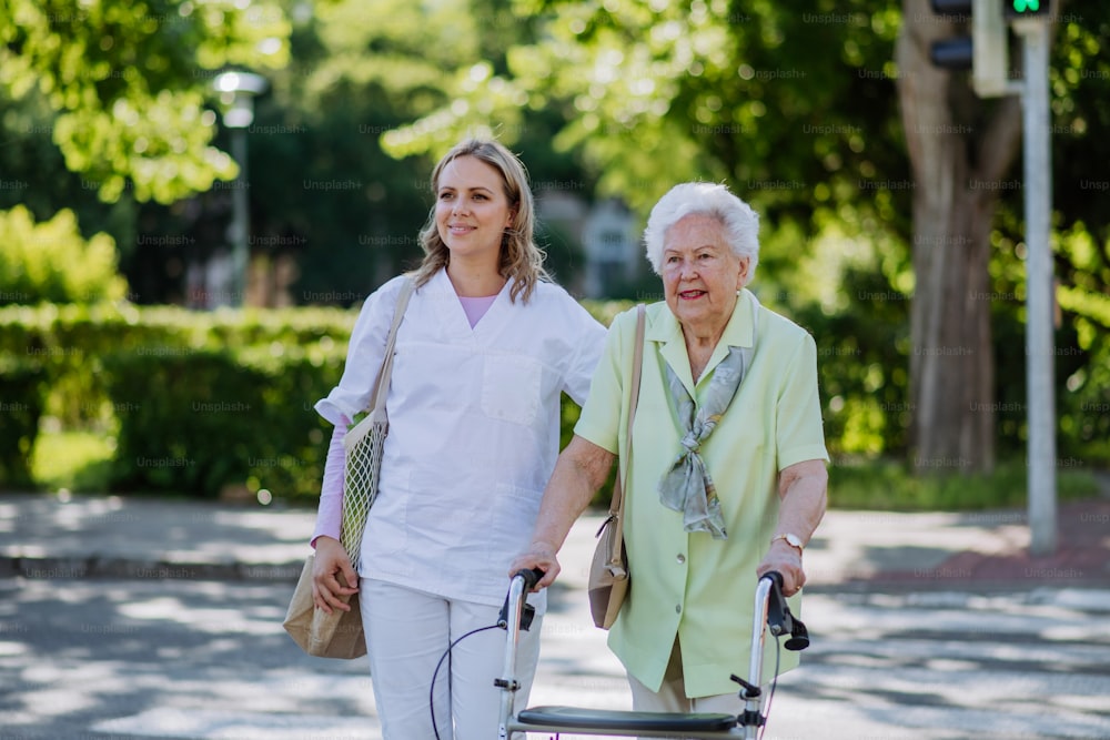 介護者と年配の女性が散歩し、公園で買い物袋を持った歩行器。