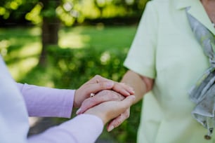 A close-up of caregiver consoling senior woman and touching her hand in park in summer.