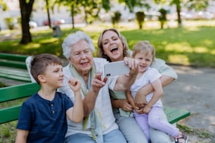 A great grandmother taking selfie with her granddaughter and kids when sitting in park in summer.
