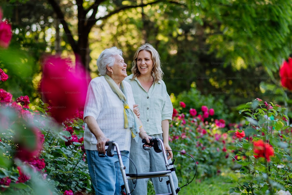Una abuela adulta que apoya a su abuela mayor cuando la lleva a caminar con un andador en el parque en verano.