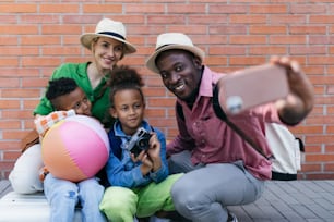 Multiracial family travelling together with small kids. Taking selfie in front of a brick wall.