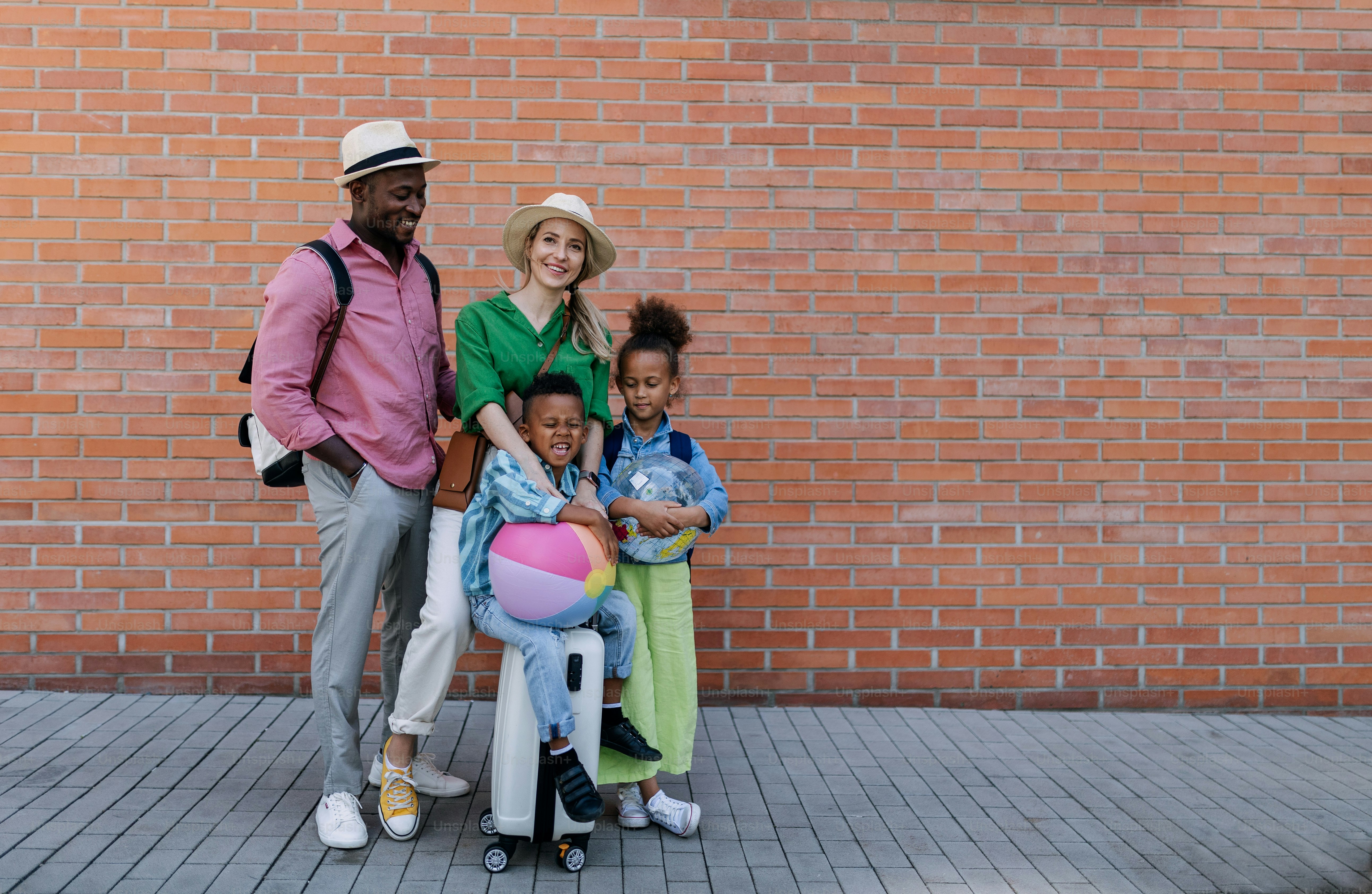 Multiracial family travelling together with small kids. Posing in front of a brick wall.