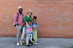 小さな子供と一緒に旅行する多民族の家族。レンガの壁の前でポーズをとる。