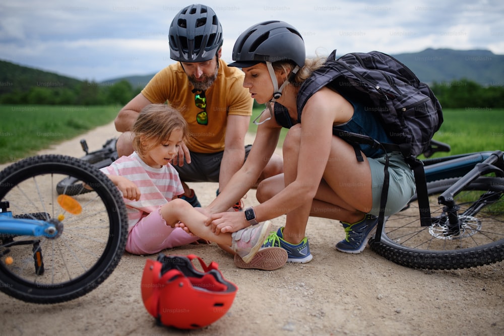 A mother and father helping their little daughter after falling off bicycle outdoors