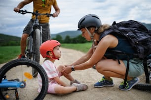 Una madre y un padre ayudan a su pequeña hija después de caerse de la bicicleta al aire libre