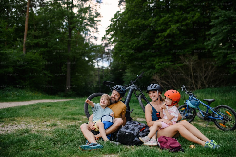 Una familia joven con niños pequeños descansando después de un paseo en bicicleta, sentados en el césped en el parque en verano.