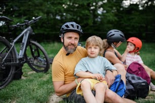 �자전거를 타고 쉬고 있는 어린 아이들을 둔 젊은 가족, 여름에 공원의 잔디밭에 앉아 있다.